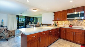 A modern kitchen with wooden cabinets, a stainless steel microwave, and a large island with a sink. - Kamaole Sands 10-205  Ocean View, Fountain View, Great Location, Great Rates! (Kihei)