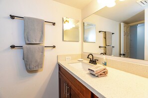 A bathroom with a sink, mirror, towel rack, and a door leading to another room.