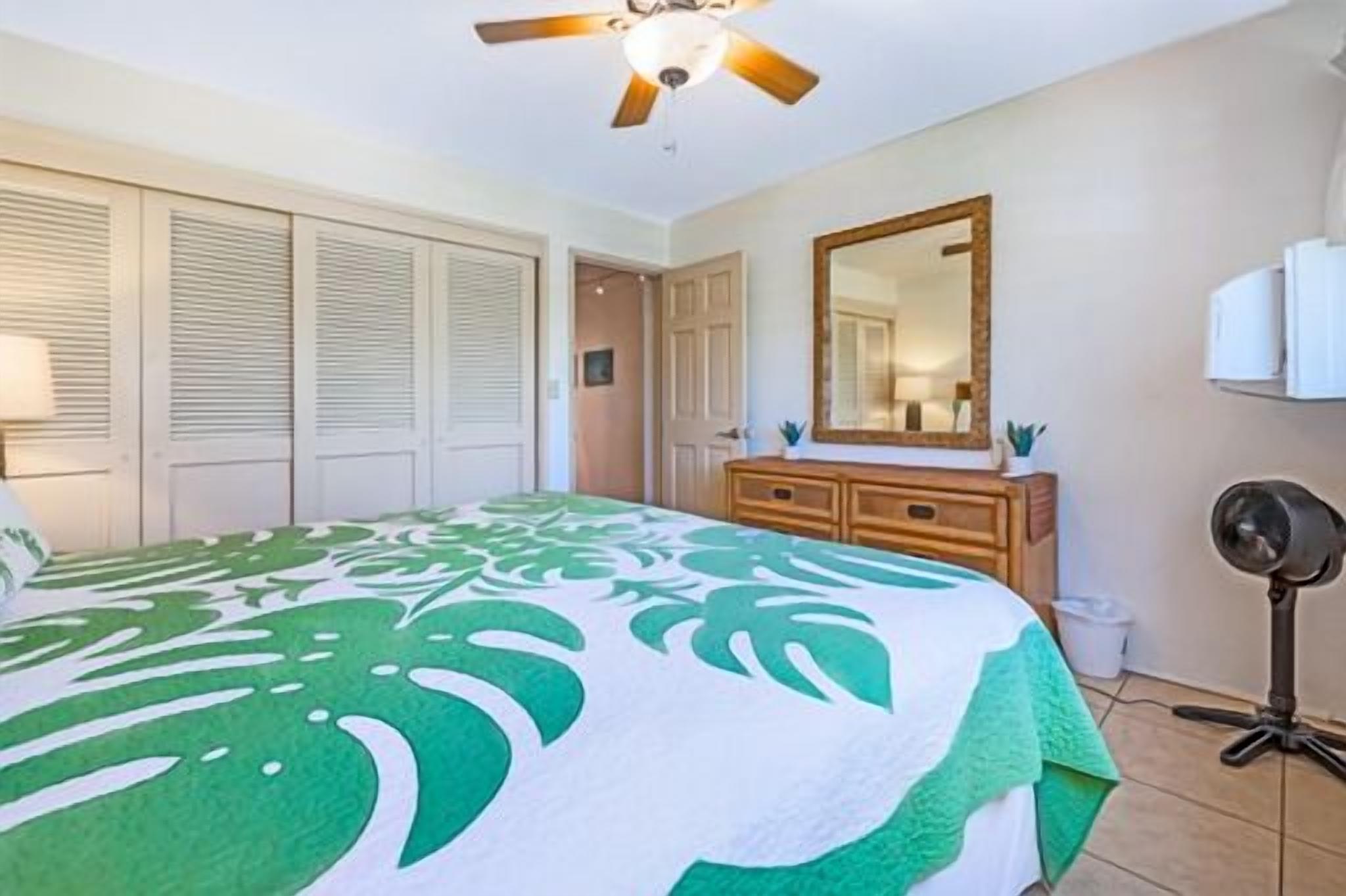 A bedroom with a bed, a ceiling fan, a dresser, a mirror, and a fan on a tripod.