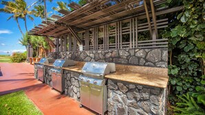 An outdoor barbecue area with stone walls and wooden pergolas, featuring two built-in grills.