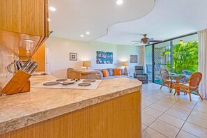 A modern kitchen with a marble countertop, wooden cabinets, and a dining area with a glass table and chairs.