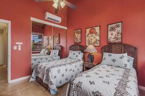 Une chambre avec deux lits, un ventilateur de plafond et des œuvres d’art accrochées aux murs.