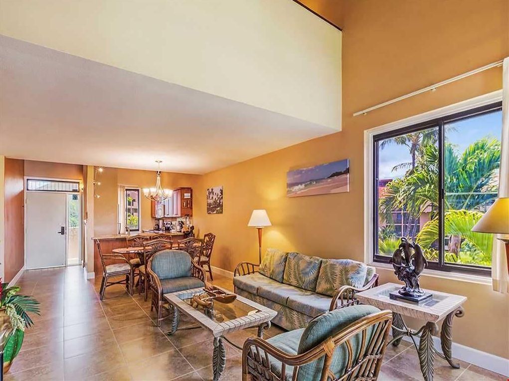 A spacious living area with a dining table, chairs, a sofa, and a coffee table. There is a large window with a view of greenery outside.