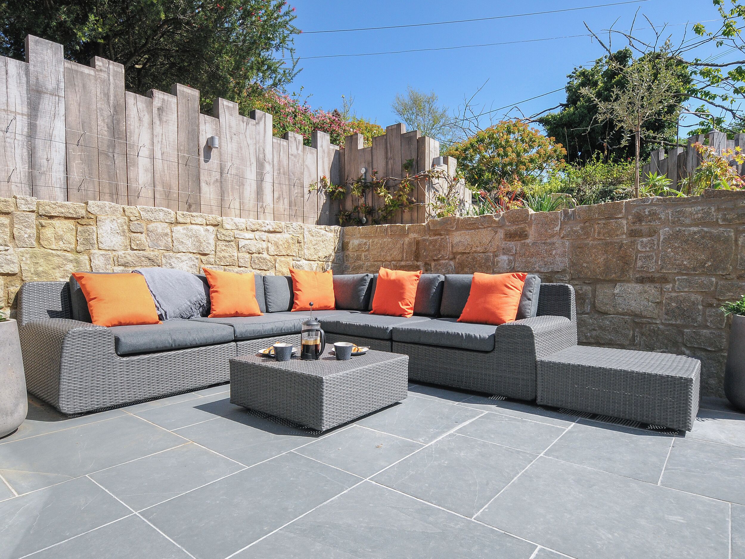 Ein Ecksofa mit orangefarbenen und grauen Kissen, ein Couchtisch und eine Wand aus Stein.