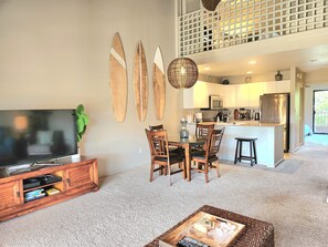 A living room with a TV, wooden chairs, a coffee table, and a kitchen area with a fridge and microwave.