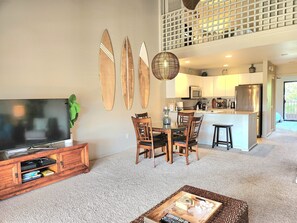 Una sala de estar con televisor, sillas de madera, una mesa de centro y una cocina con refrigerador y microondas.