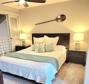 A bedroom with a bed, two bedside tables, a ceiling fan, and a wall-mounted lamp.
