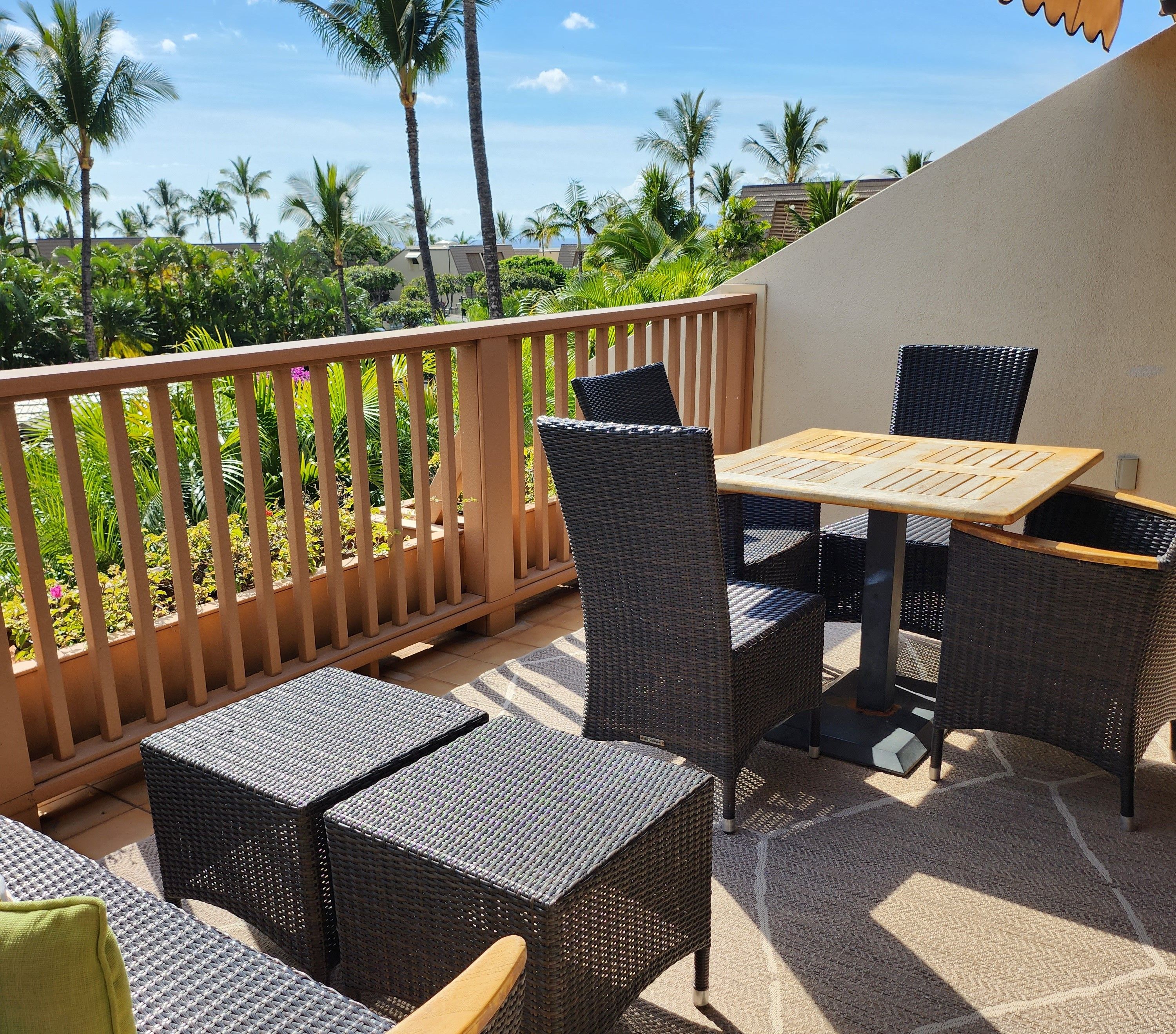A patio with wicker furniture, a wooden table, and a view of palm trees and buildings.