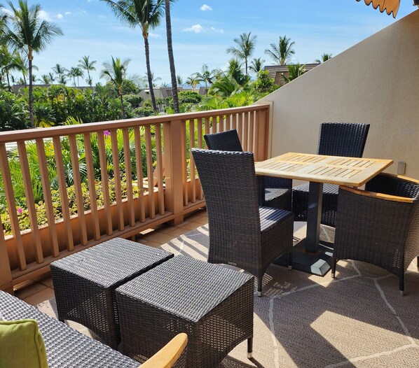 A patio with wicker furniture, a wooden table, and a view of palm trees and buildings.