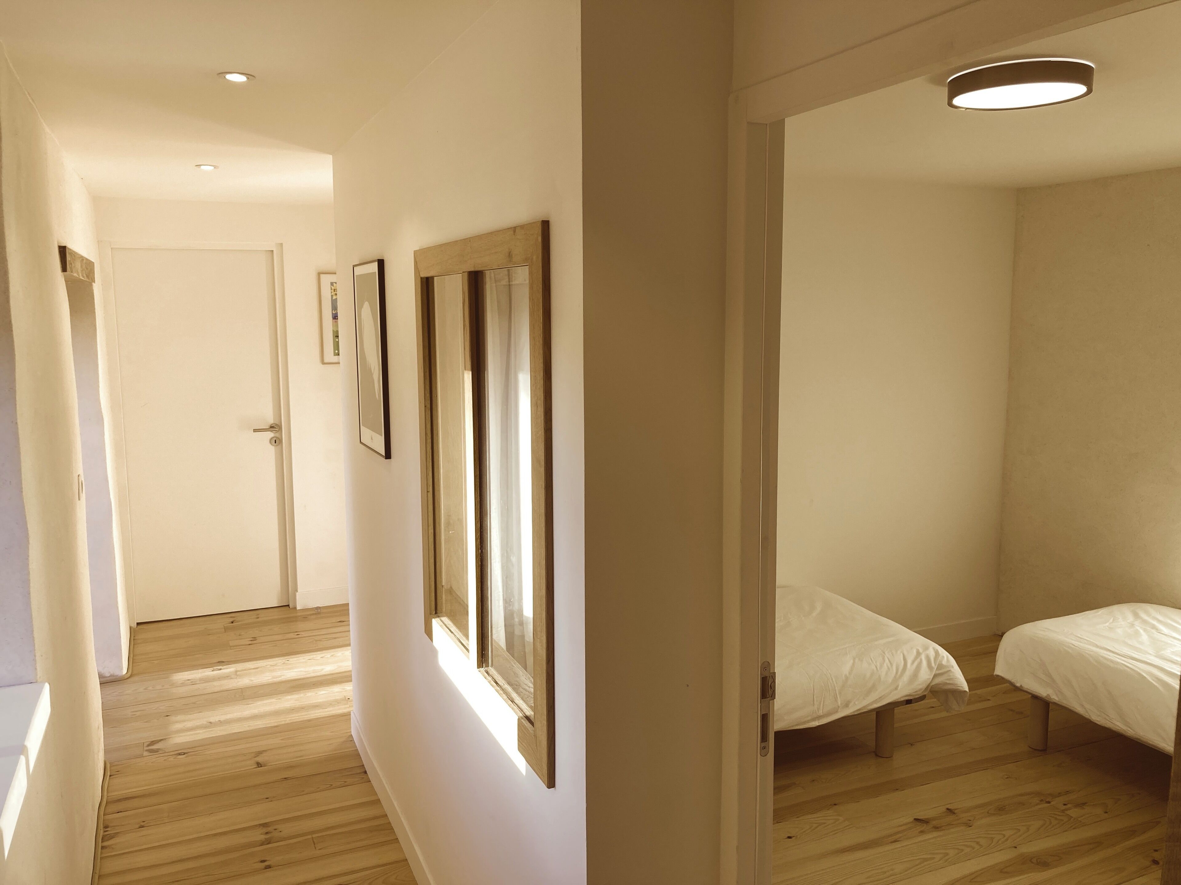 A bedroom with a wooden floor, a bed, and a door leading to another room.