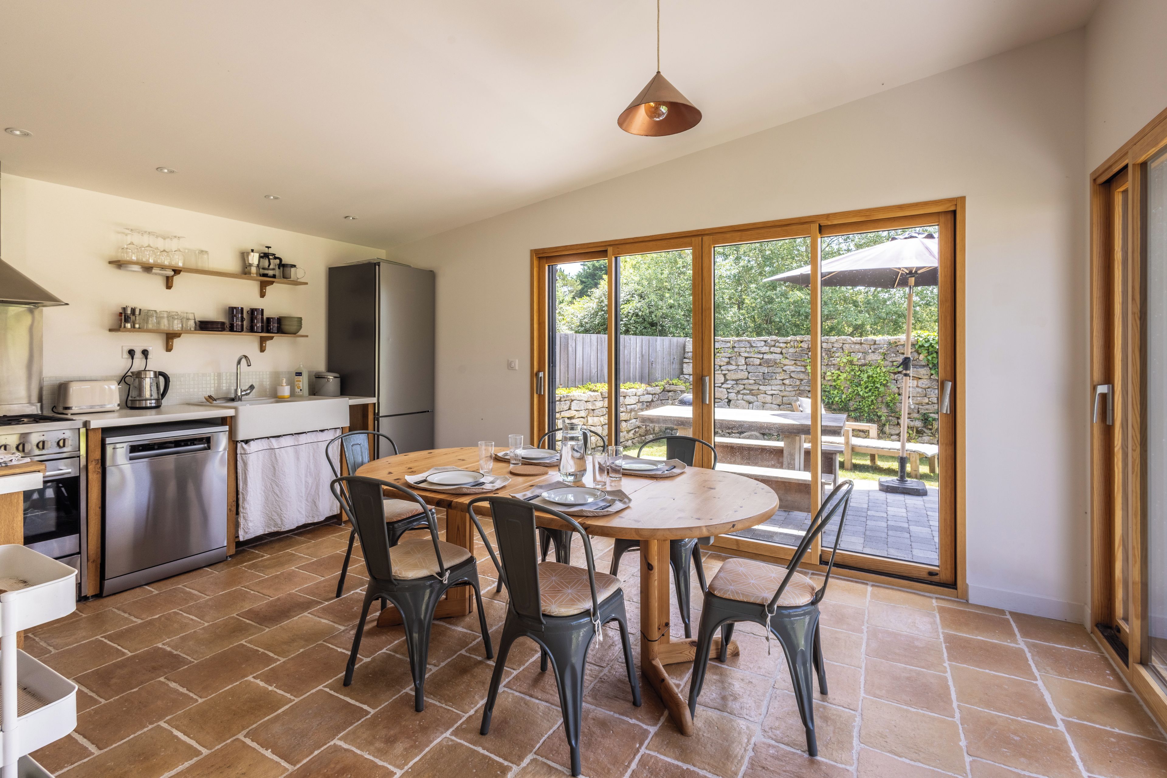 Eine moderne Küche mit Edelstahlgeräten, ein Essbereich mit einem runden Tisch und eine große Schiebeglastür, die auf eine Terrasse im Freien führt.