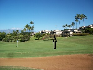 A golf course with a clubhouse in the background, surrounded by palm trees and a clear sky. - Wailea Ekolu #306 Panoramic Ocean Views on Wailea Golf Course, Wifi, A/C (Wailea)