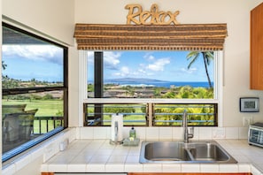 A kitchen with a large window overlooking a golf course and ocean, a sink, and a 'Relax' sign above the window. - Wailea Ekolu #306 Panoramic Ocean Views on Wailea Golf Course, Wifi, A/C (Wailea)