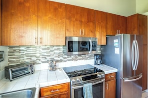 A modern kitchen with wooden cabinets, a stainless steel refrigerator, a microwave, a toaster, and a stove. - Wailea Ekolu #306 Panoramic Ocean Views on Wailea Golf Course, Wifi, A/C (Wailea)