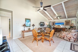 A spacious living room with a high ceiling, a dining area with wicker chairs, a sofa with a tropical print, and a large painting of a beach scene. - Wailea Ekolu #306 Panoramic Ocean Views on Wailea Golf Course, Wifi, A/C (Wailea)