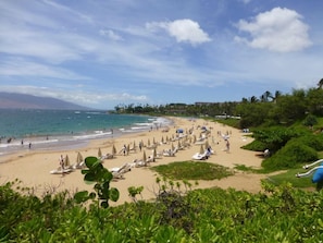 A beach with numerous umbrellas and lounge chairs, a clear sky, and a view of the ocean. - Wailea Ekolu #306 Panoramic Ocean Views on Wailea Golf Course, Wifi, A/C (Wailea)
