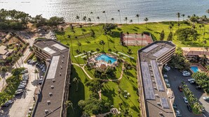 Eine Luftaufnahme eines Resorts mit einem zentralen Pool, umgeben von gepflegten Rasenflächen und Palmen, mit Strand und Ozean im Hintergrund.