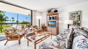 Ein Wohnzimmer mit Sofa, Sesseln, Couchtisch, Fernseher und Bücherregal.