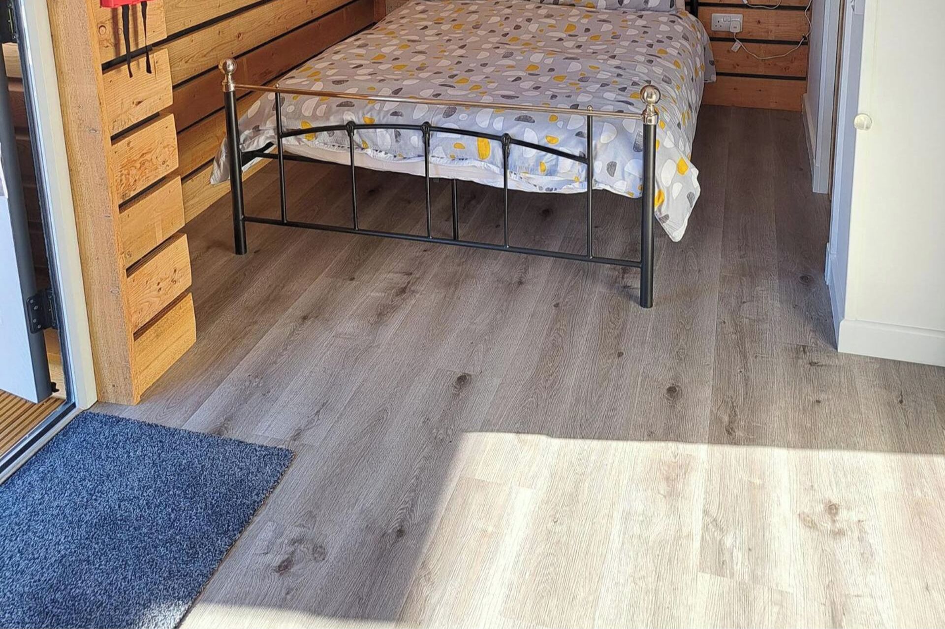 A bedroom with a bed, wooden walls, and a wooden floor.