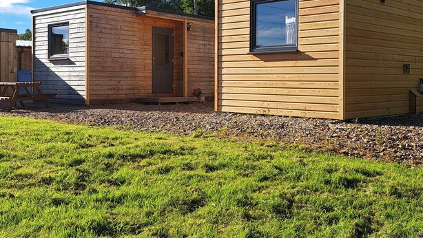 A row of wooden cabins with a grassy foreground and trees in the background.
