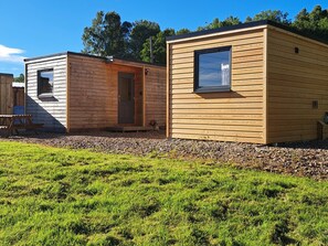 A row of wooden cabins with a grassy foreground and trees in the background. - The Posh Bothy Spean Bridge (Roybridge)