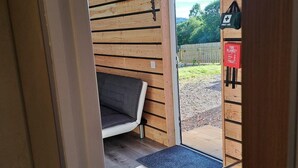 A wooden interior with a bed, a first aid kit, and a fire blanket on the wall.