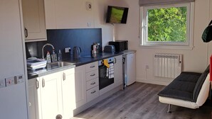 A compact kitchen with a sink, microwave, kettle, and a TV mounted on the wall.