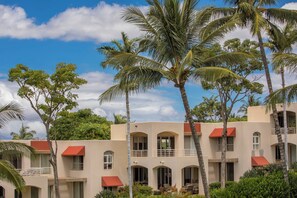 A multi-story building with balconies, surrounded by palm trees and greenery.
