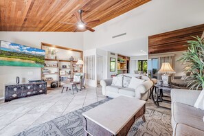 A spacious living room with a ceiling fan, a large painting, a sofa, a coffee table, and a bookshelf.