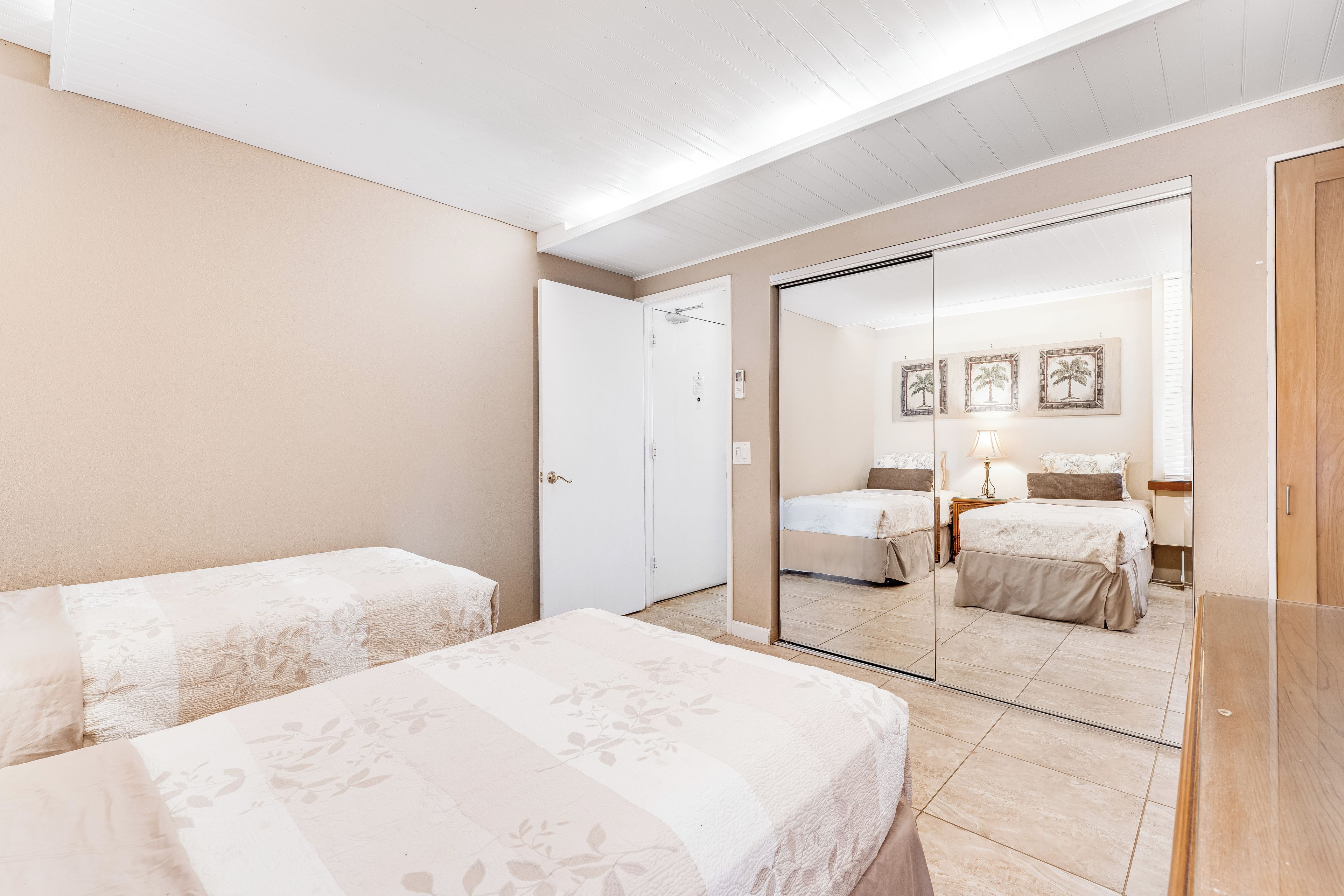 A hotel room with two beds, a large mirror, and a door leading to another room.