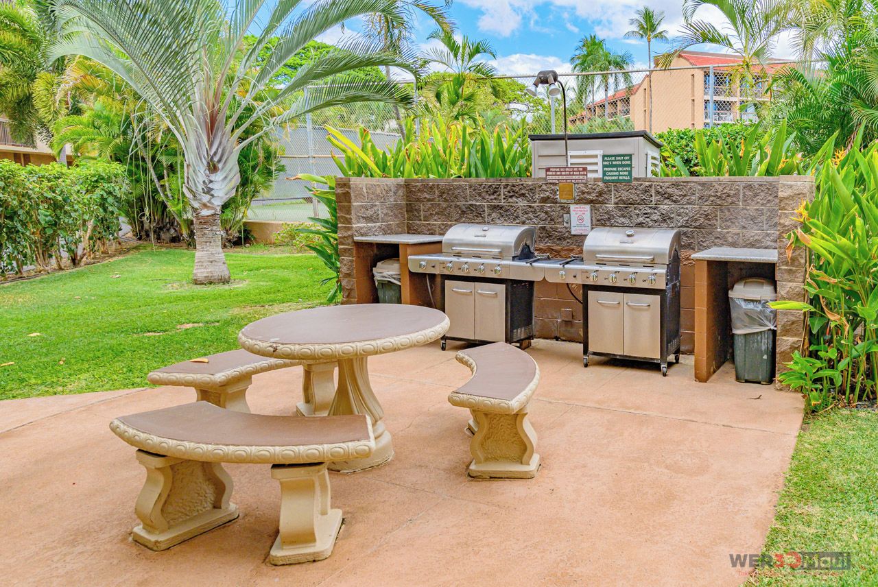 An outdoor kitchen with a grill, a table, and benches.