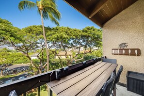 Une terrasse en bois avec une table et des chaises, donnant sur un quartier résidentiel bordé d’arbres et où sont garées des voitures.