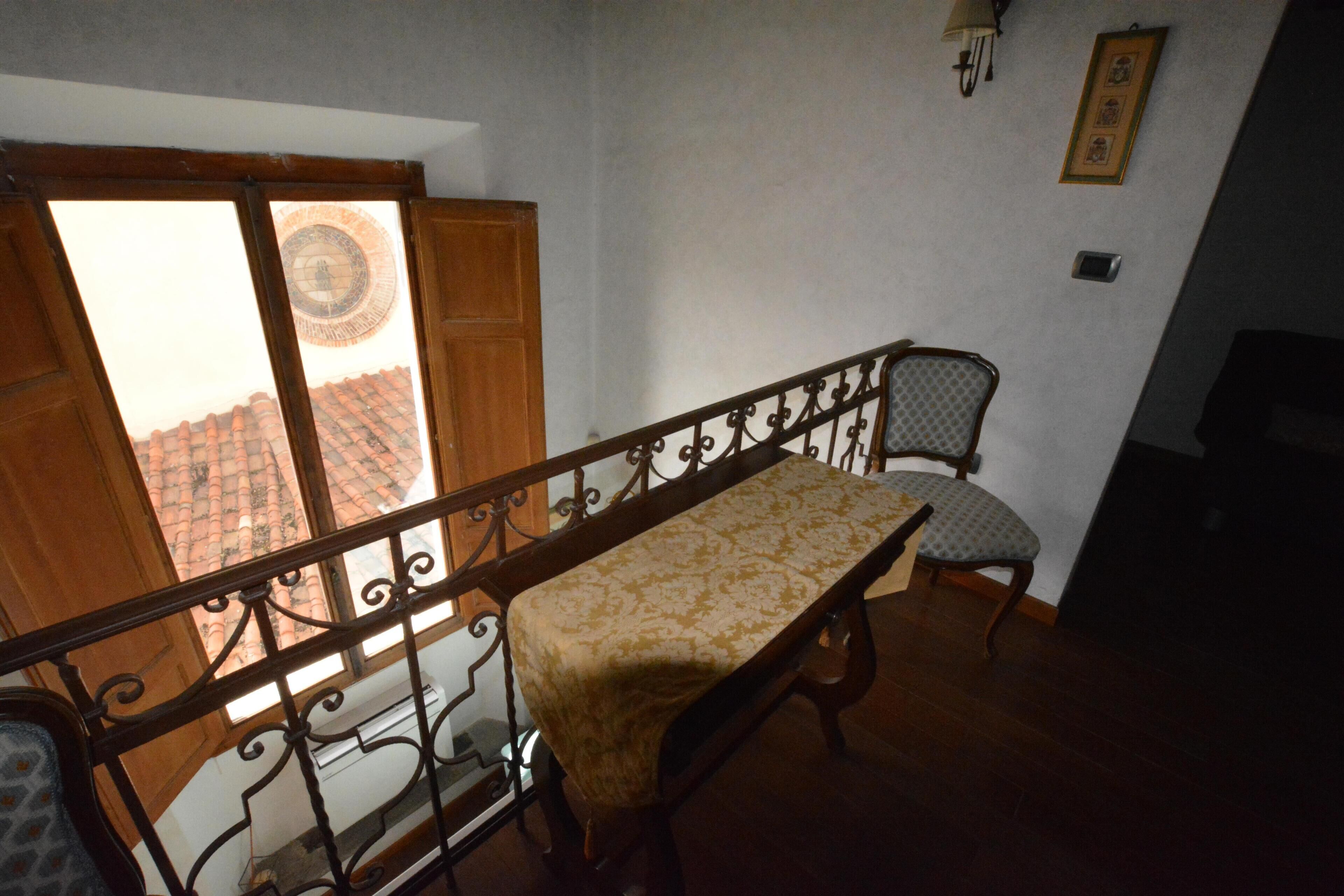 Habitació amb llit, una cadira, finestra que mostra un teulat llostre i una làmpada penjada a la paret.