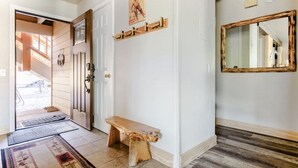 Un pasillo con un banco de madera, un perchero, un espejo y una puerta que da a una escalera.