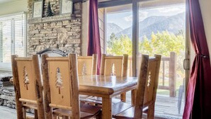 Una mesa de madera con seis sillas, una pared de piedra con cuadros enmarcados y vistas a las montañas a través de un ventanal.