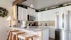 Una cocina moderna con armarios blancos, un refrigerador de acero inoxidable y una isla de madera con taburetes.
