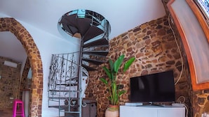 Un escalier en colimaçon dans une pièce rustique aux murs de pierre, avec un téléviseur et un meuble.