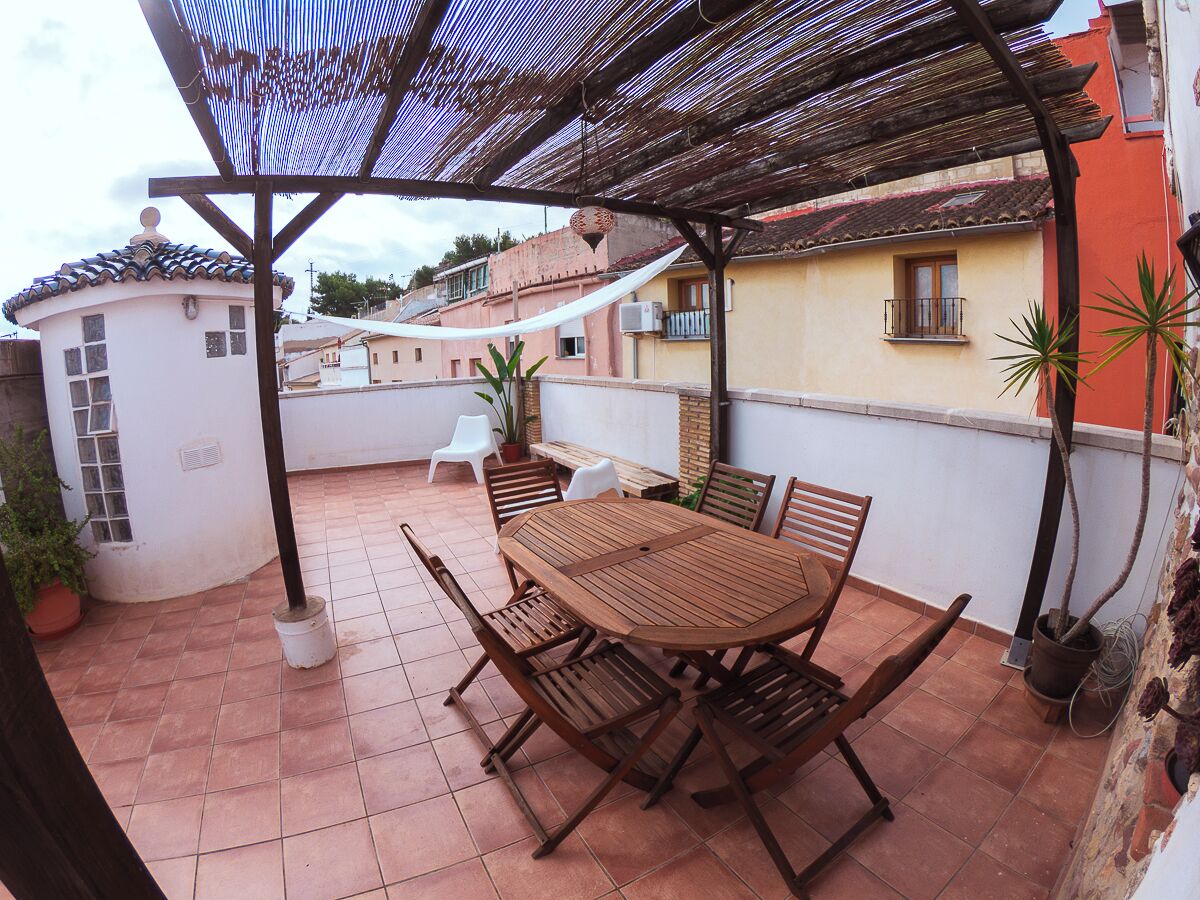Une terrasse couverte avec une table et des chaises en bois, des plantes en pot et une chaise blanche.