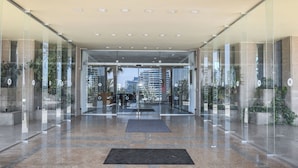 Entrada moderna de hotel con puertas de cristal, suelo de baldosas y vista del paisaje urbano al fondo.