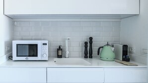 Una cocina con microondas blanco, hervidor y pileta.