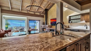 A spacious kitchen with a large granite countertop, a built-in stove, and a view of the ocean through large windows.