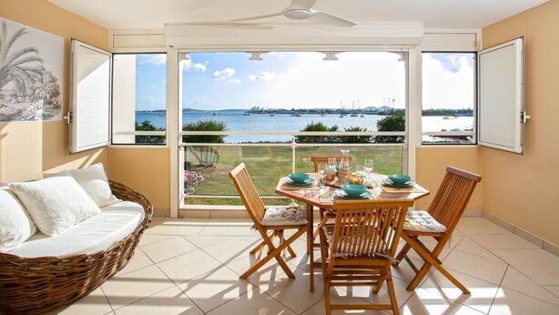 Un balcon avec une table dressée pour le dîner, un canapé en osier et une vue sur la mer et les bateaux.