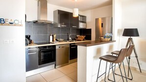 Une cuisine moderne dotée d’un îlot central, d’appareils électroménagers en acier inoxydable et d’un luminaire suspendu.