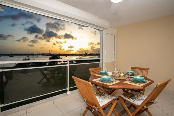 A dining area with a table set for four, overlooking a marina with boats and a sunset view.