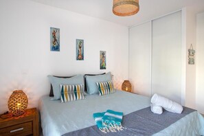 A bedroom with a bed, pillows, a blanket, a lamp, and artwork on the wall.