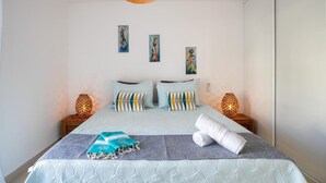 Un lit bien fait, recouvert d’une couvre-lit à motifs bleus et blancs, avec deux oreillers et une serviette pliée posée sur une table de chevet en bois.