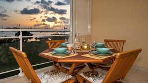 Une table à manger dressée pour quatre personnes, agrémentée de touches de bleu sarcelle et d’or, placée près d’une grande fenêtre donnant sur une marina au coucher du soleil.