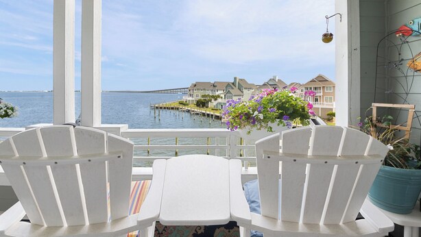Blick auf das Meer von einer Veranda mit weißen Stühlen und einem Tisch, mit Blick auf einen Steg und Häuser.