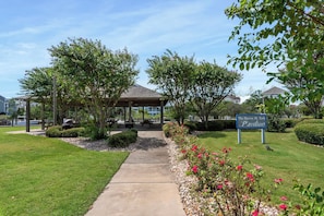 A pathway leading to a gazebo with picnic tables, surrounded by well-maintained grass and flowering plants. - The Hook: Waterfront | Boat Slip | Shared Pool (Manteo)