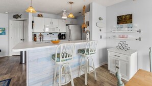 Eine moderne Küche mit weißen Schränken, einer zentralen Kochinsel mit Barhocker, Pendelleuchten und einem Deckenventilator.